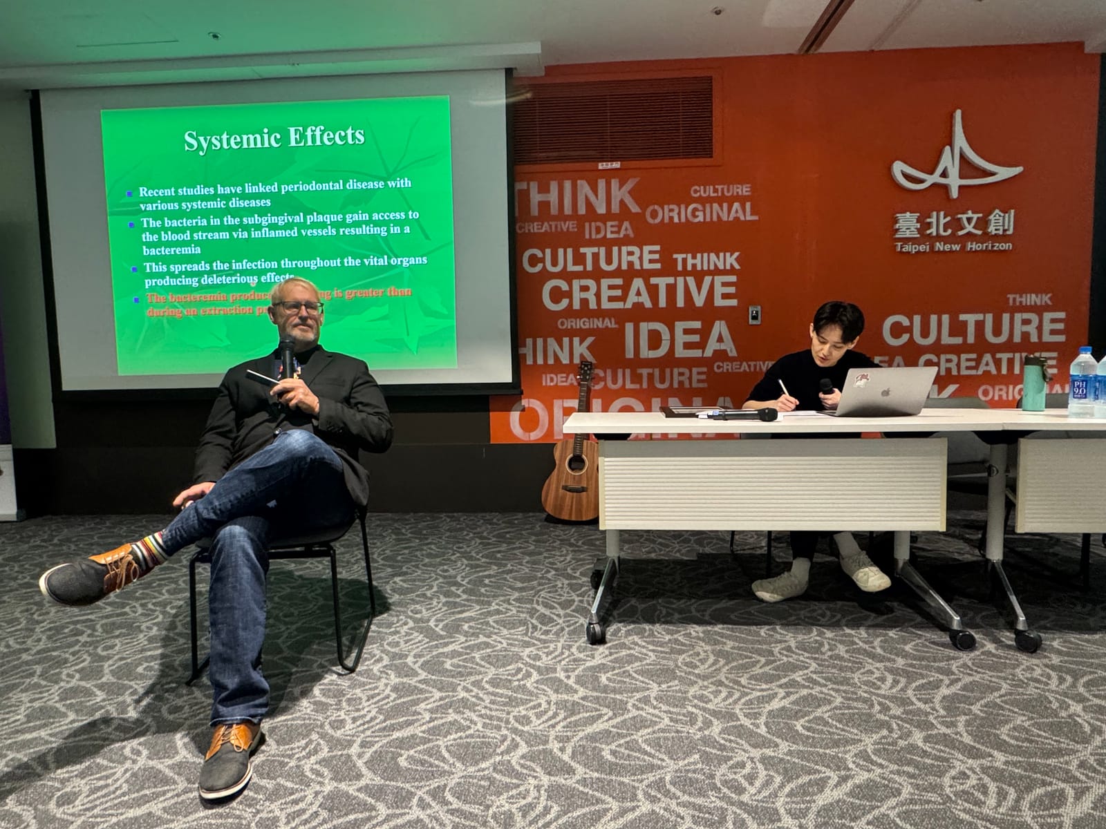 Dr. Brook Niemiec 坐在投影片 Systemic Effects 前講解