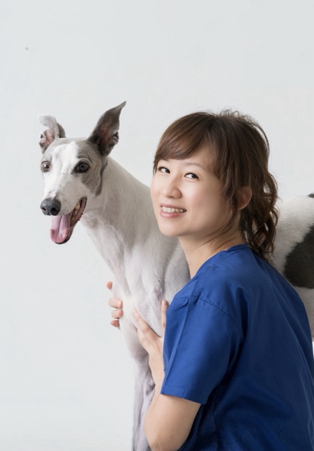 蔡依津獸醫師與一隻靈緹犬的合照，她穿著藍色刷手服，回頭微笑。